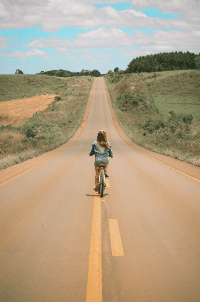 Menina andando de bicicleta em estrada. Foto de luizph, Pexels.