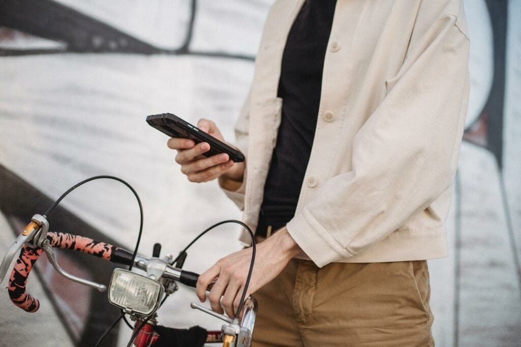 Homem, segurando o celular com uma mão e guidão da bike com a outra mão - Foto: Pexels
